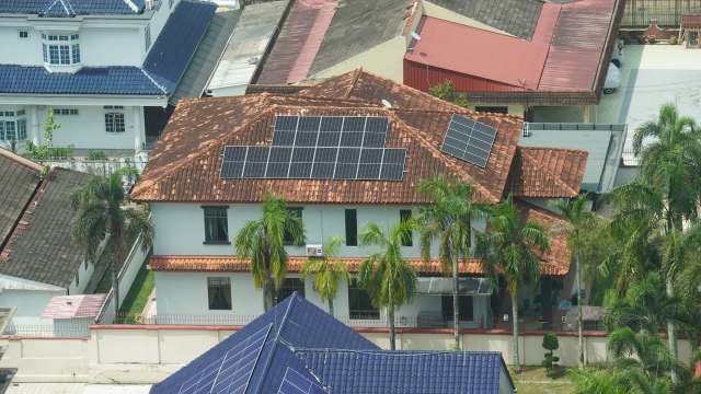 A residential building with a tiled roof and solar panels, surrounded by palm trees and other rooftops.