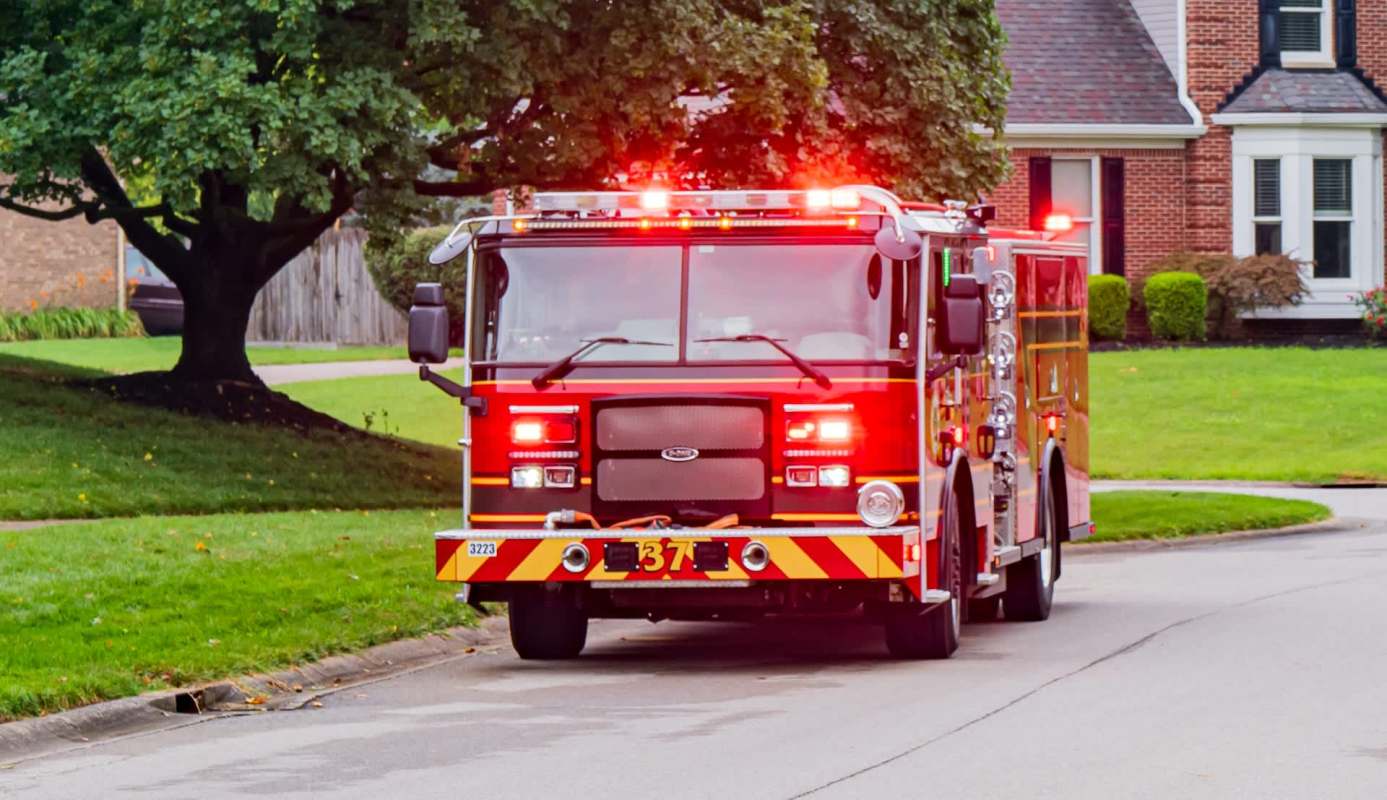 A fire truck with flashing lights parked on a residential street near a house and trees.