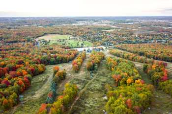 Aerial view of vibrant autumn foliage over fields and residential areas.