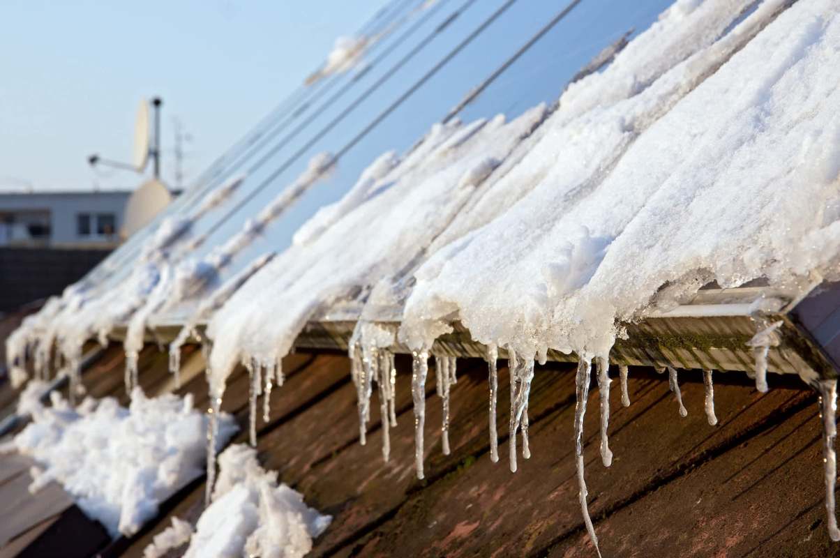Snow and icicles on a roof with solar panels.