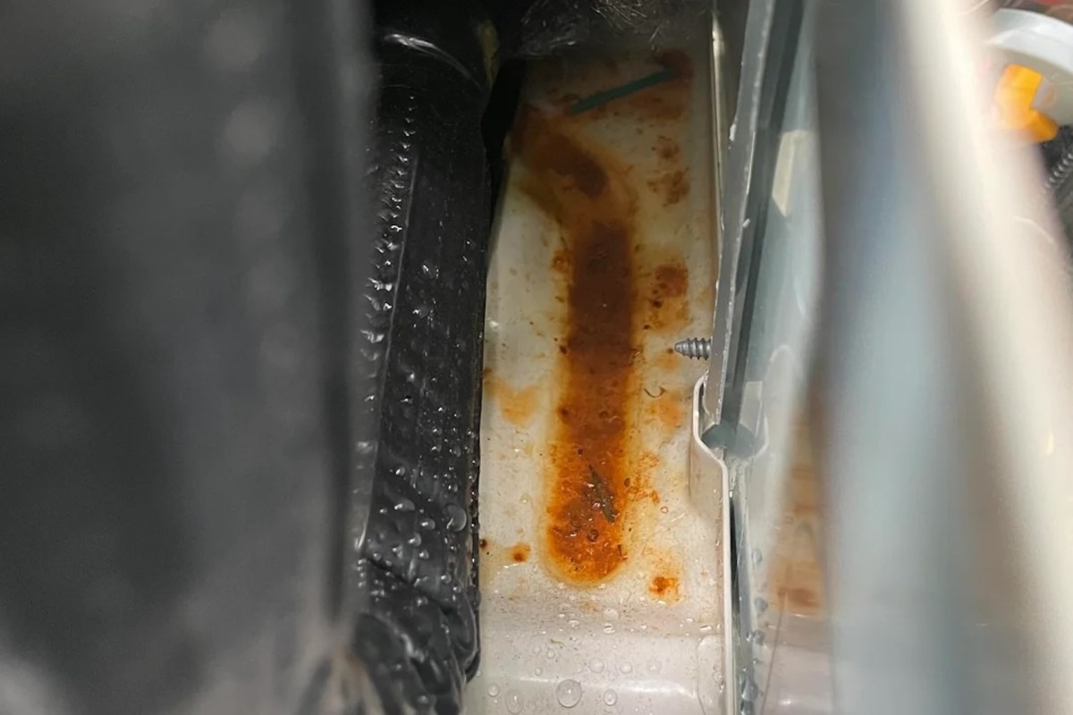 A rust-stained surface with droplets of water, showing a metal screw and surrounding black material.
