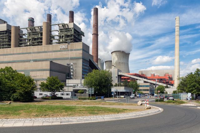 A RWE power plant with cooling towers and multiple chimneys under a blue sky with scattered clouds.