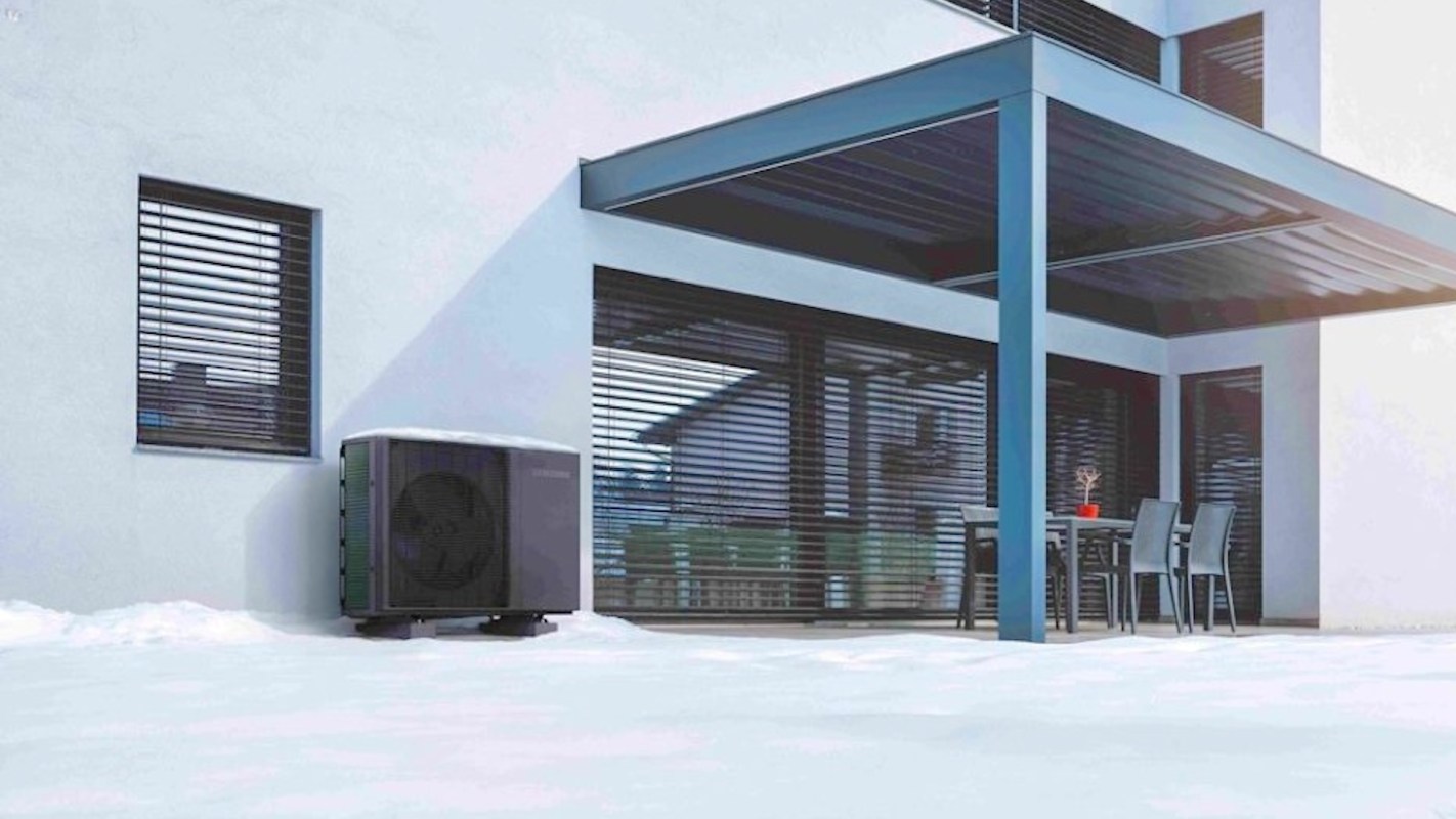 A heat pump unit beside a house with a covered patio and snow on the ground.