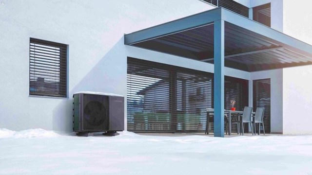 A heat pump unit beside a house with a covered patio and snow on the ground.