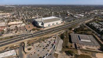An aerial view of the Alamodome in San Antonio next to a highway with surrounding buildings and parking areas.