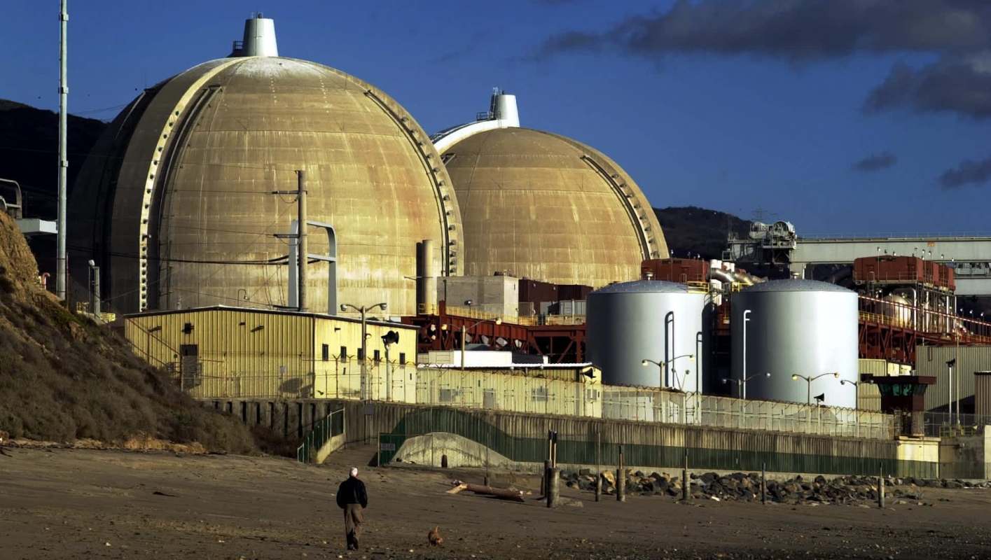 A nuclear power plant with large domes and storage tanks near a beach.