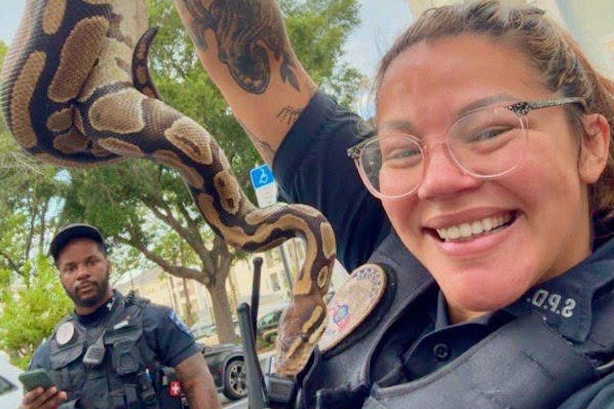 Two police officers are outside; one holds a snake while the other looks at a phone.