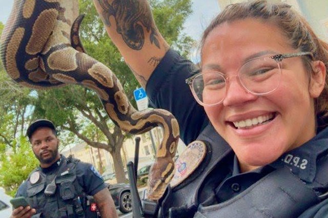 Two police officers are outside; one holds a snake while the other looks at a phone.