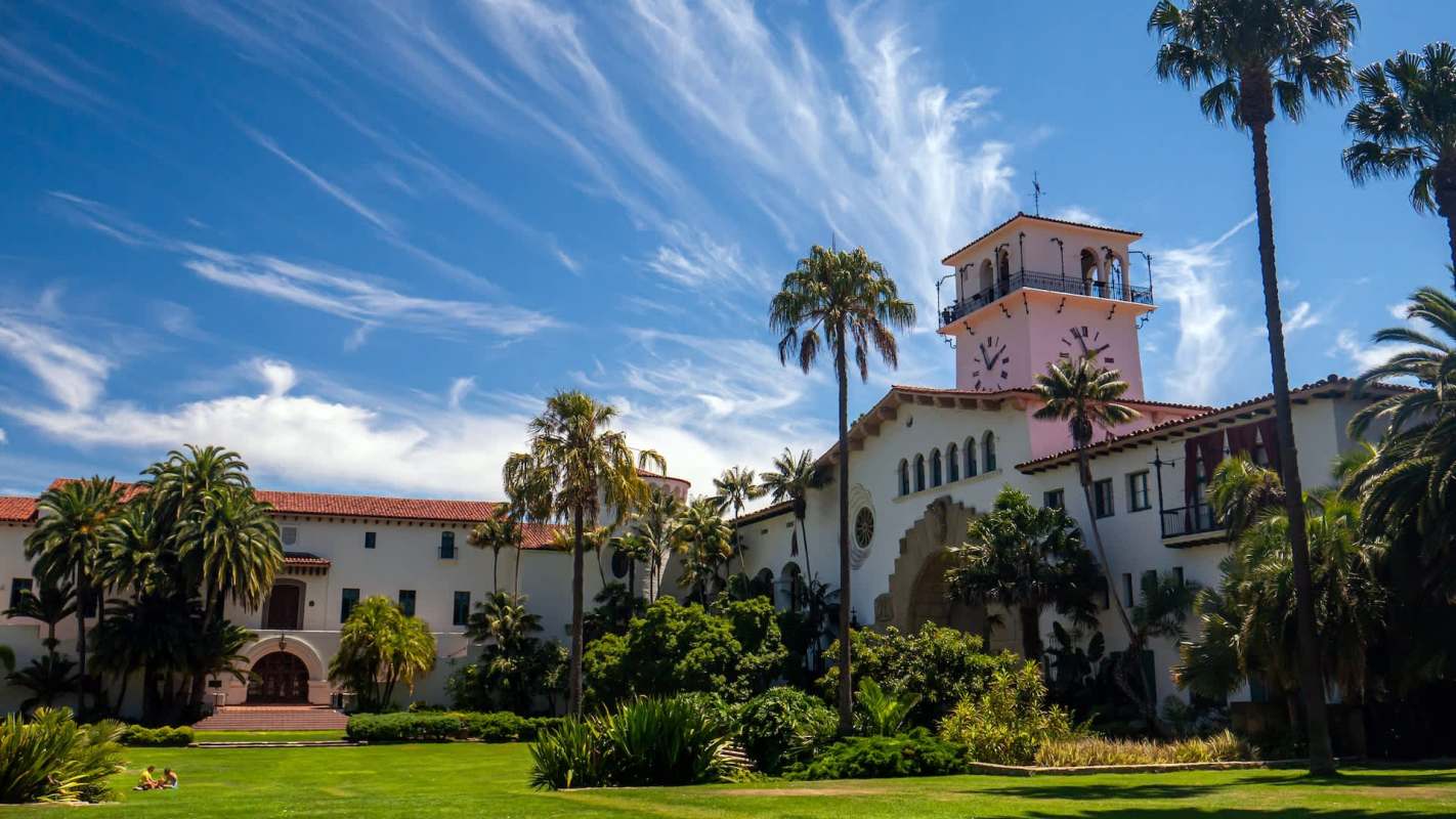 A large building with a clock tower surrounded by palm trees and a green lawn.
