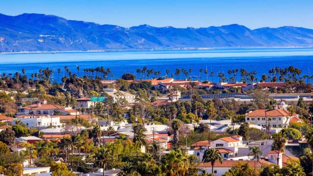 Santa Barbara, California, with red-tiled rooftops and palm trees, overlooking the ocean and mountains in the background.