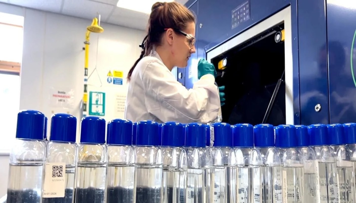 A woman in a laboratory using equipment with rows of sample bottles in the foreground.
