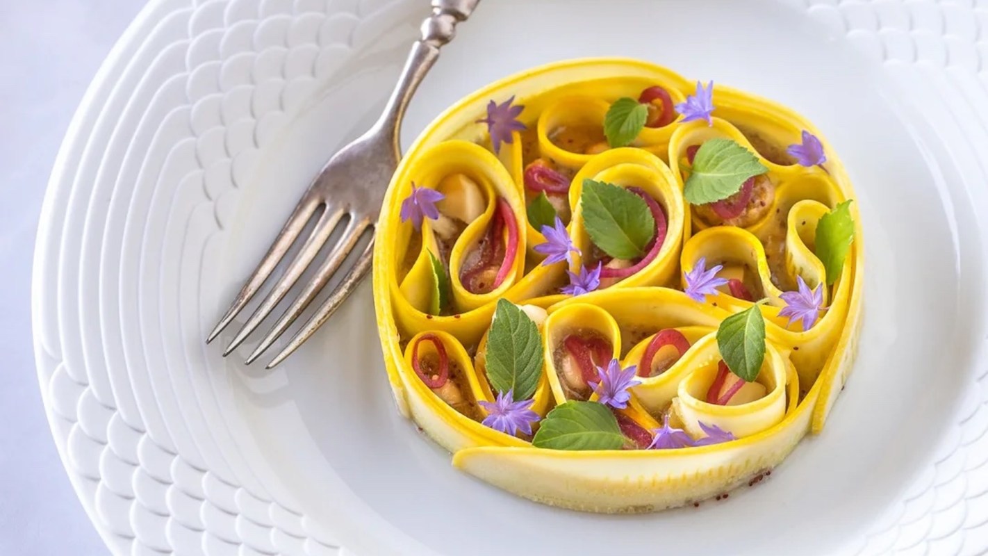 A decorative plate of rolled pasta garnished with herbs and edible flowers.