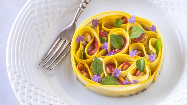 A decorative plate of rolled pasta garnished with herbs and edible flowers.