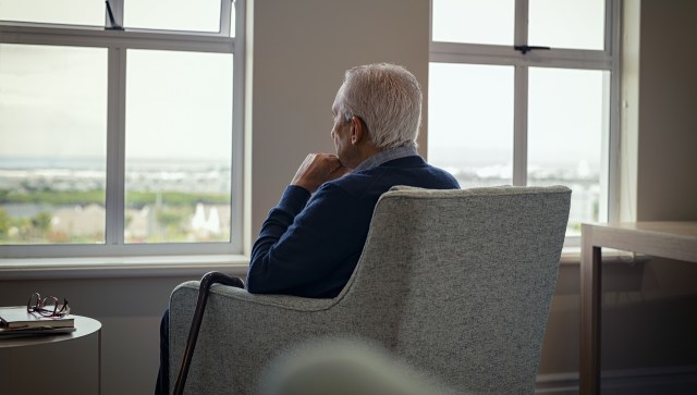 An older man seated in an armchair, looking out a window at a distant landscape.