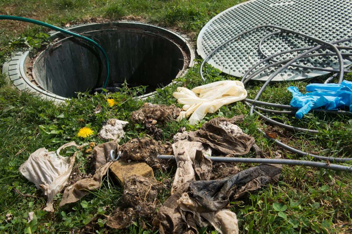 A manhole surrounded by various types of debris and gloves on the grass.