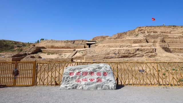 An archaeological site with terraced ruins and a sign in front of a wooden gate.