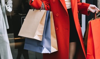 A person holding multiple shopping bags while wearing a red coat.