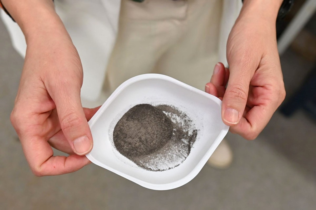 A person holds a small dish containing a mound of silver powder.