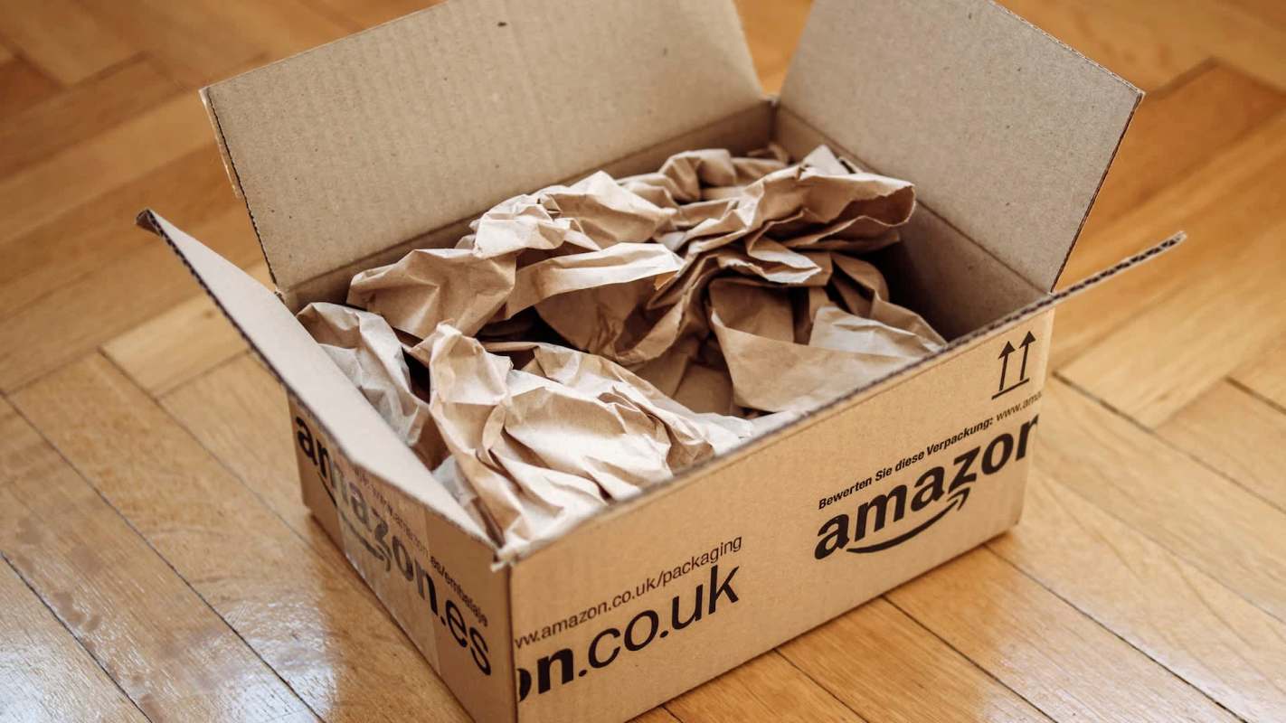 A cardboard box filled with crumpled paper sits on a wooden floor.