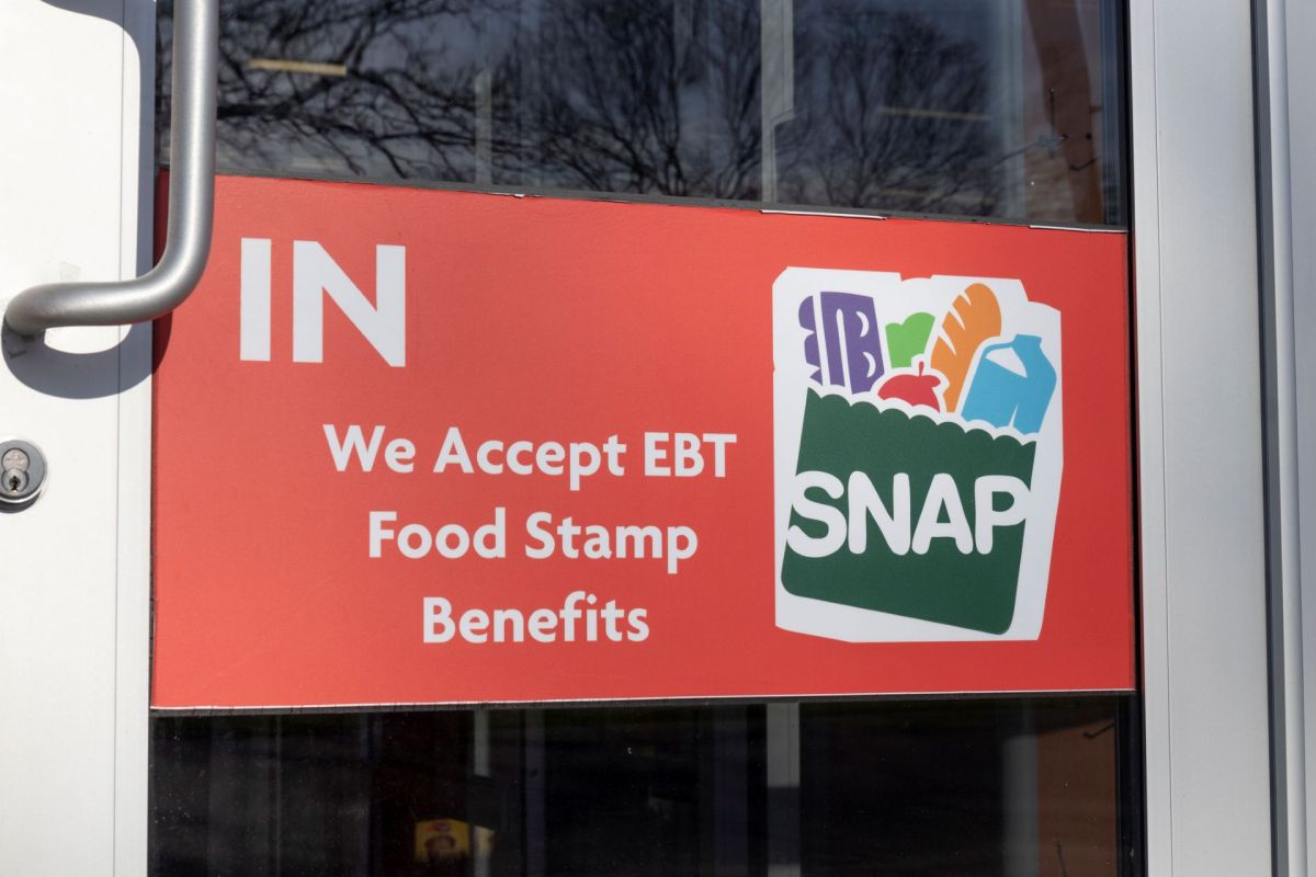 A sign on a door that reads "We Accept EBT Food Stamp Benefits" with a graphic of food items.