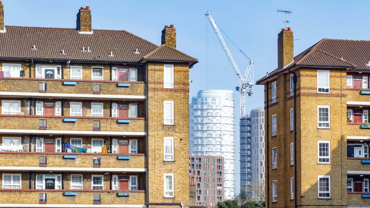 Two buildings with balconies and windows, with a construction crane and modern skyscrapers in the background.