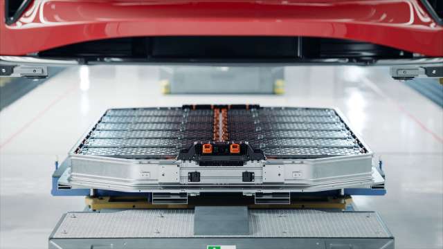 A battery pack is positioned below a red vehicle in an industrial setting.