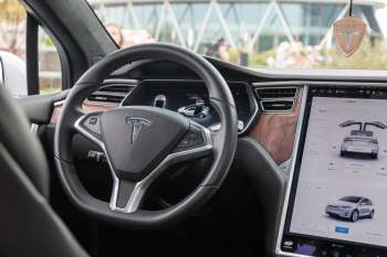 The interior of a Tesla car featuring a steering wheel, dashboard display, and control interface.