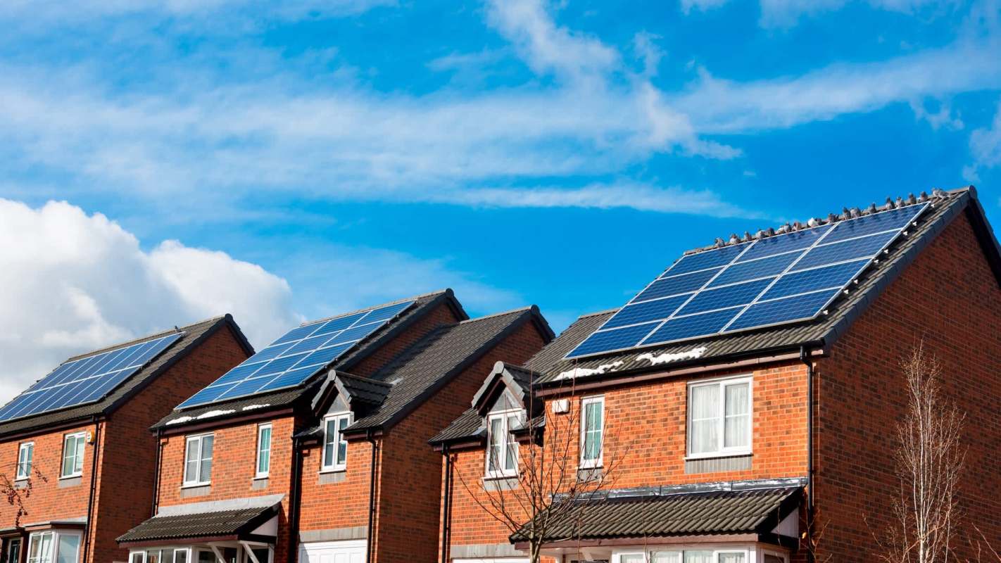 Houses with solar panels on rooftops against a blue sky with clouds.
