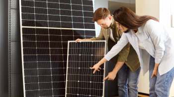 Two people examine solar panels, discussing features or specifications in a modern interior setting.