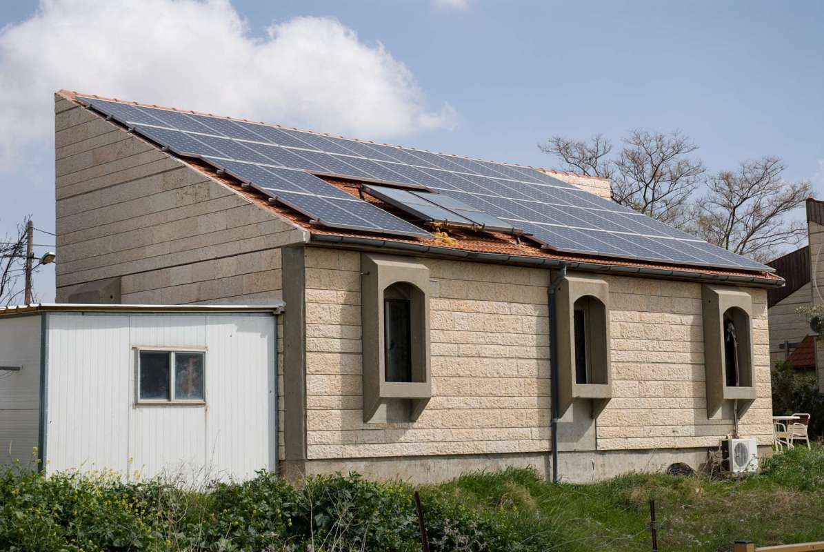 A house with solar panels on the roof and a small white shed beside it.