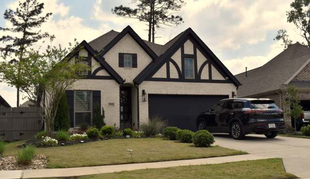 A house with a black and white exterior, a well-kept lawn, and a parked black SUV in the driveway.