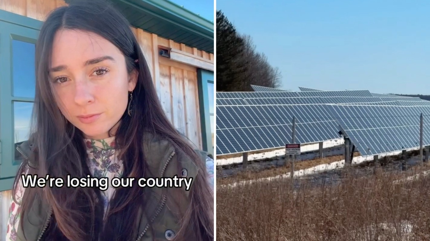 A woman stands outside a wooden building, with solar panels visible in the background.