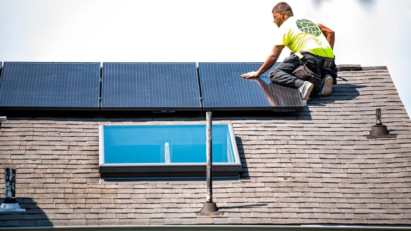 A worker installs solar panels on a sloped roof with skylights.