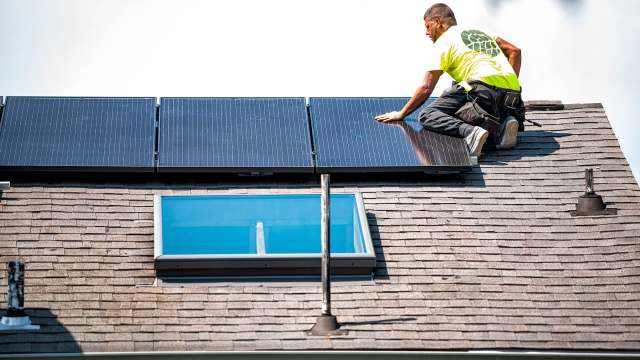 A worker installs solar panels on a sloped roof with skylights.