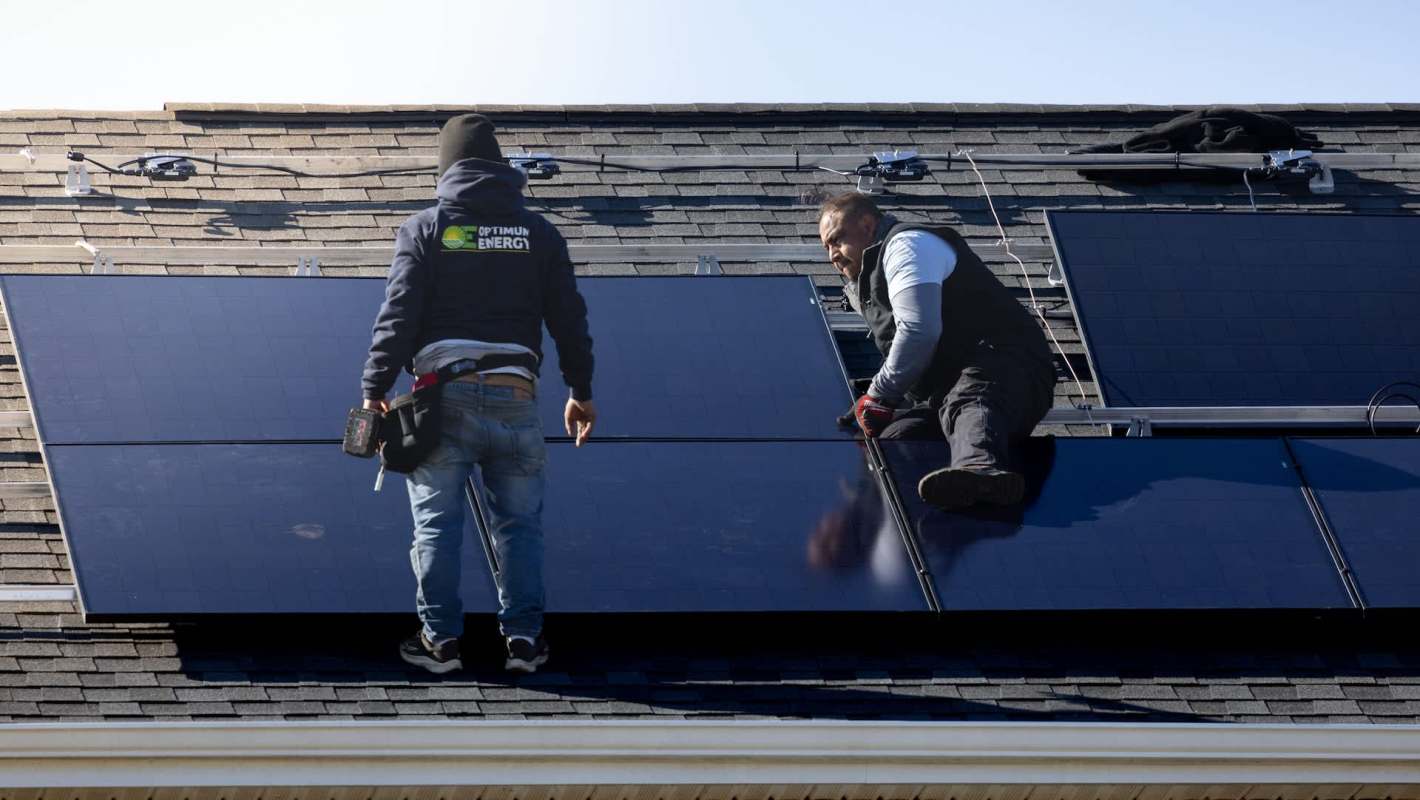 Two workers install solar panels on the roof of a house.