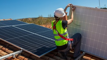 A worker installs a solar panel on a roof.