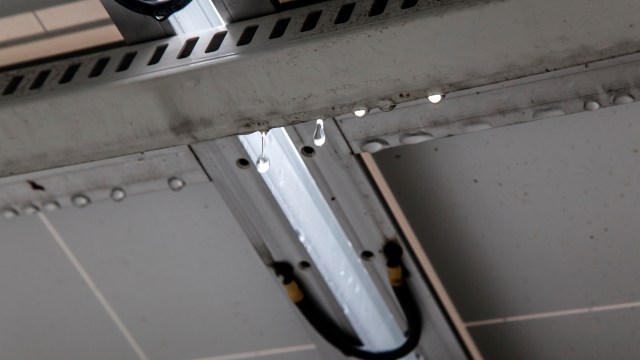 Water droplets hang from a metallic surface underneath a fluorescent light fixture.
