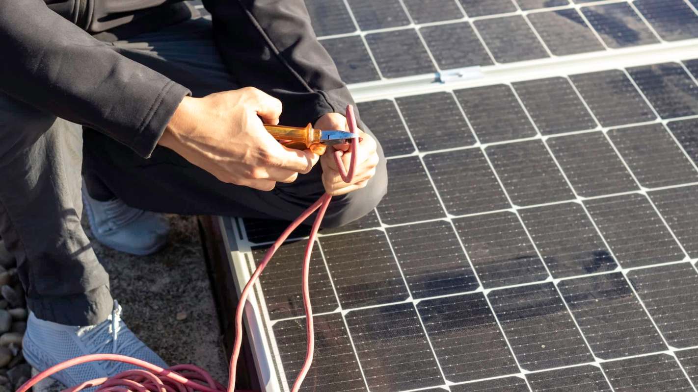 A person using a wire cutter on a solar panel cable.