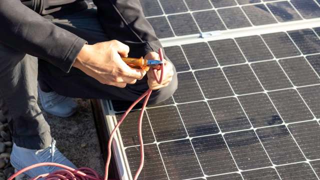 A person using a wire cutter on a solar panel cable.