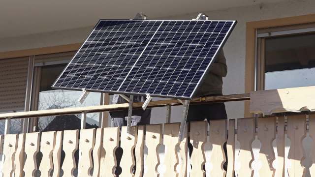 A solar panel is installed on a balcony with wooden railing.