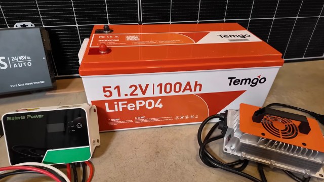 A battery and inverter in front of a solar panel.