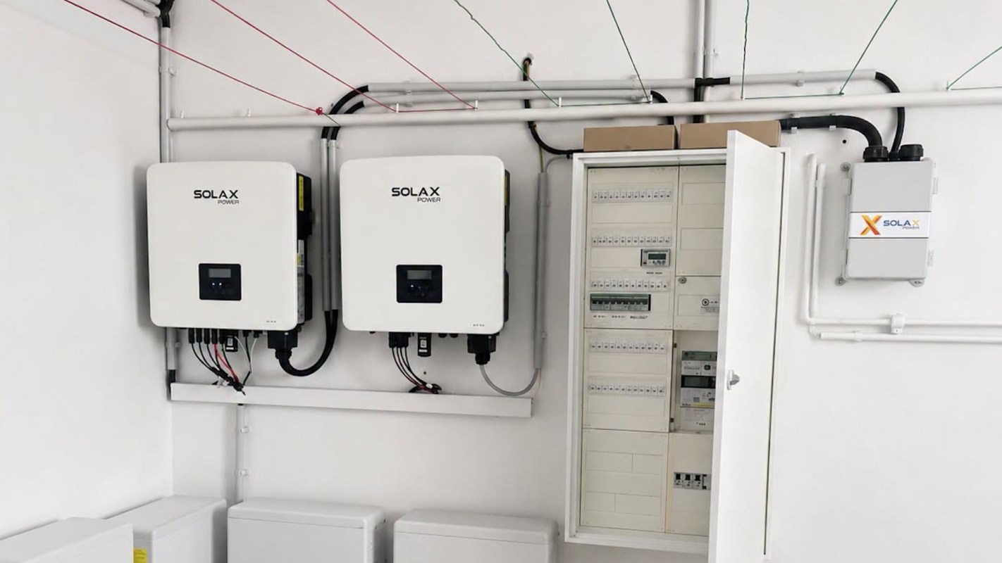 Two solar inverters mounted on a wall next to an electrical distribution panel and wiring.
