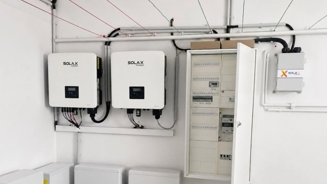 Two solar inverters mounted on a wall next to an electrical distribution panel and wiring.