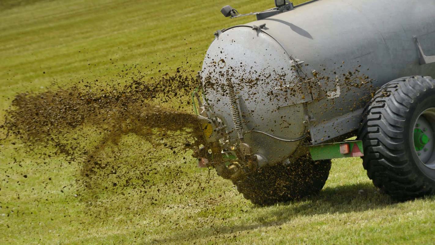 A farming machine discharges manure onto a grassy field.