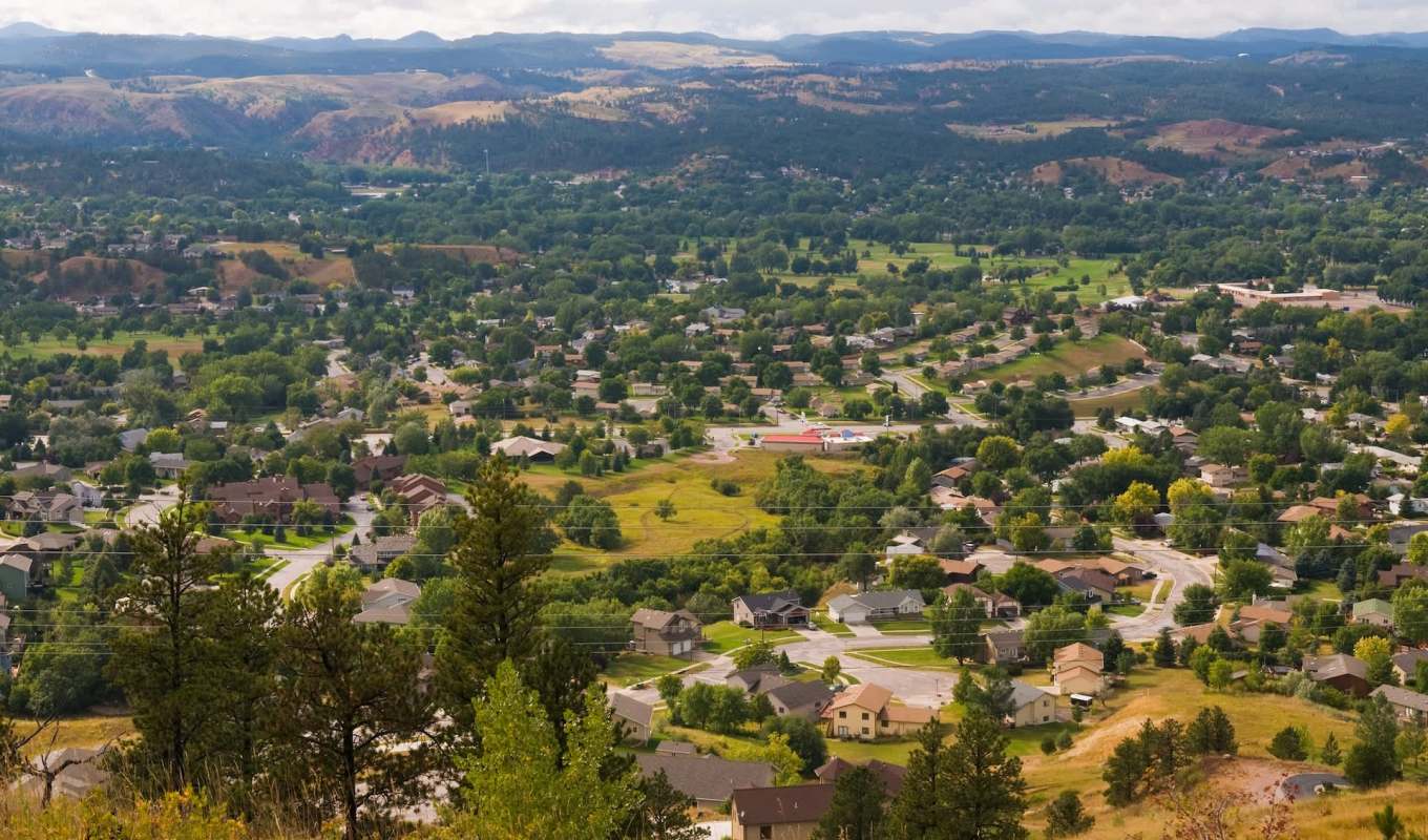 Aerial view of a neighborhood with houses, trees, and rolling hills in the background.