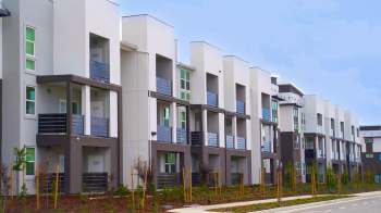 A row of modern multistory residential buildings with balconies and green landscaping.
