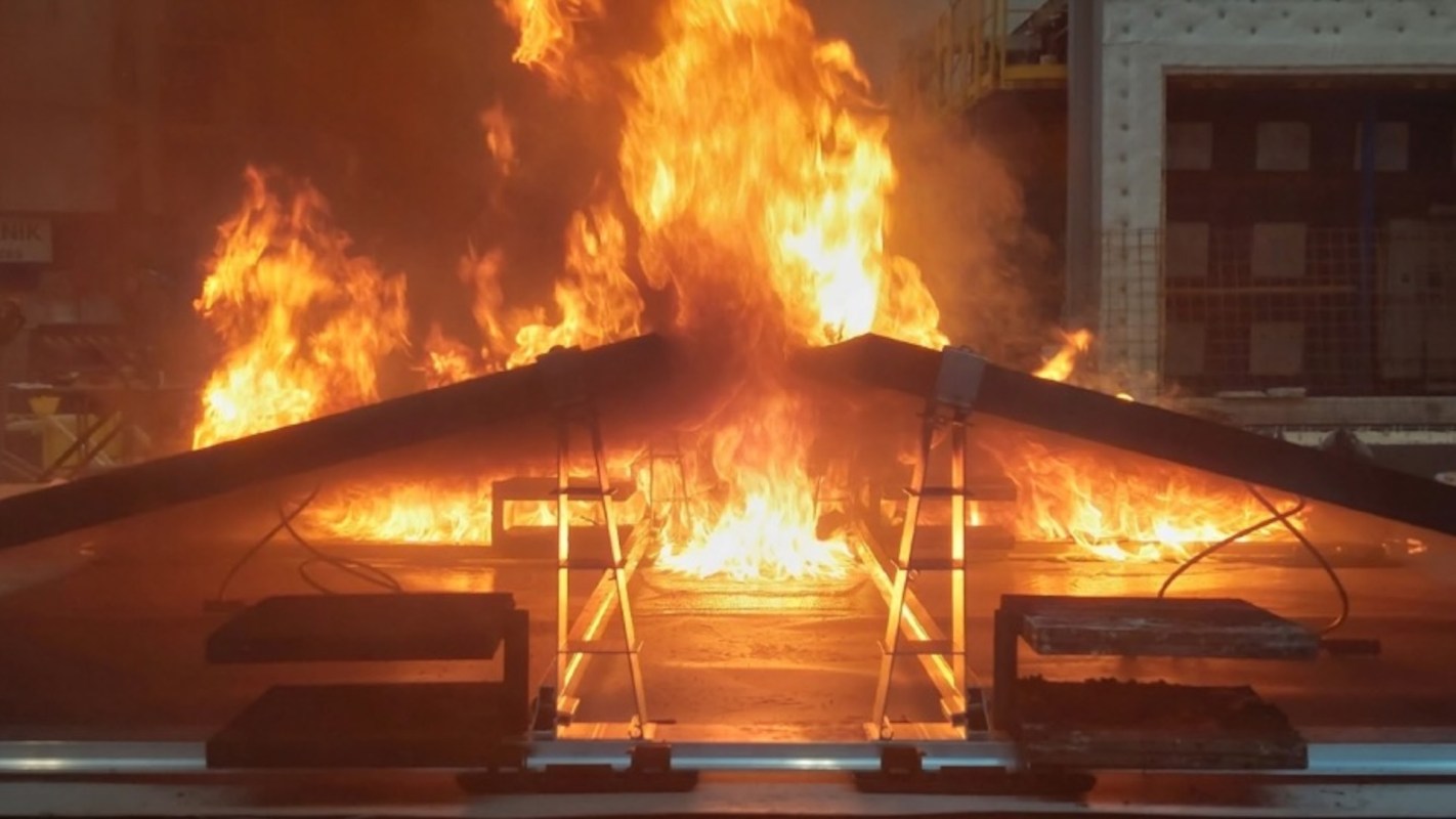 Flames engulf solar panels on metal frames in a fire test environment.