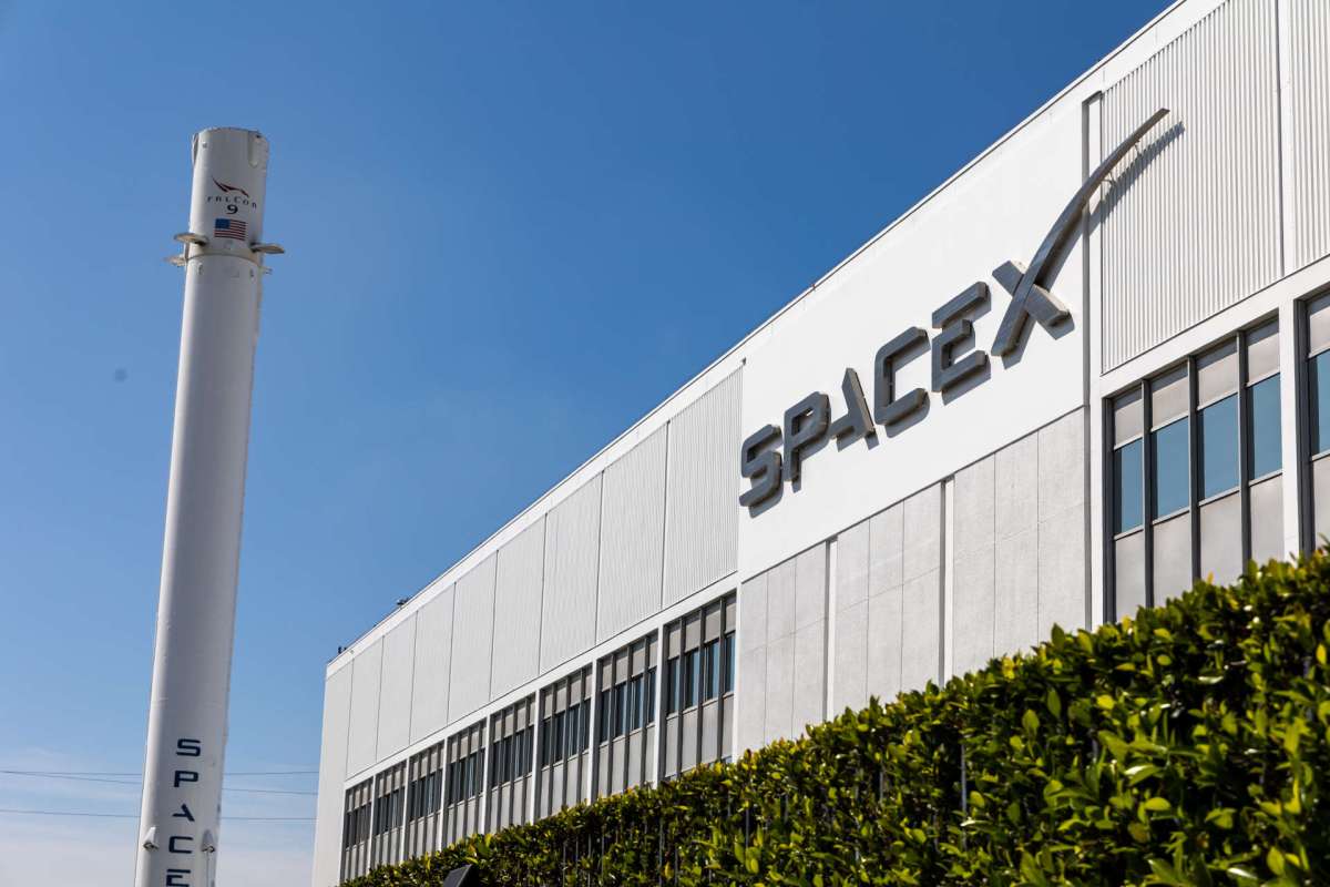 A SpaceX building with a rocket and logo visible against a blue sky.