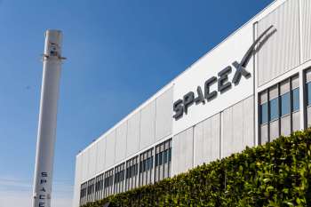 A SpaceX building with a rocket and logo visible against a blue sky.