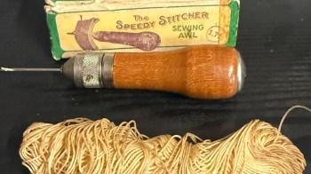 A sewing awl next to a bundle of thread and a vintage box labeled "The Speedy Stitcher Sewing Awl."